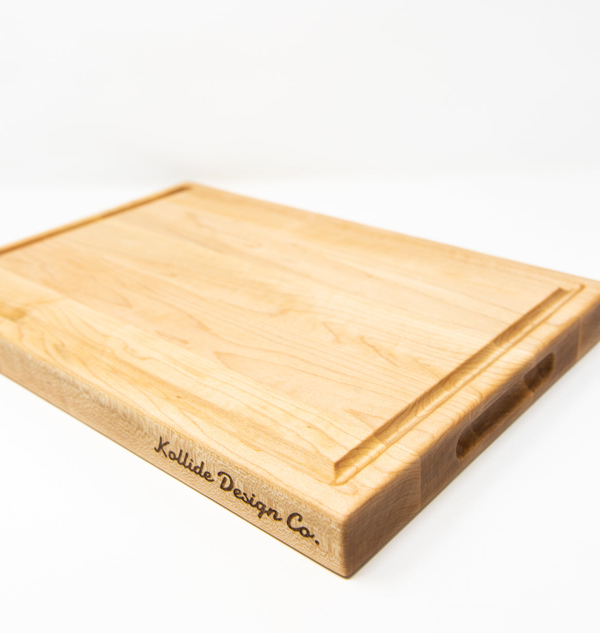 Medium size wood cutting board, made of light blonde Maple, with a juice groove and side handles.