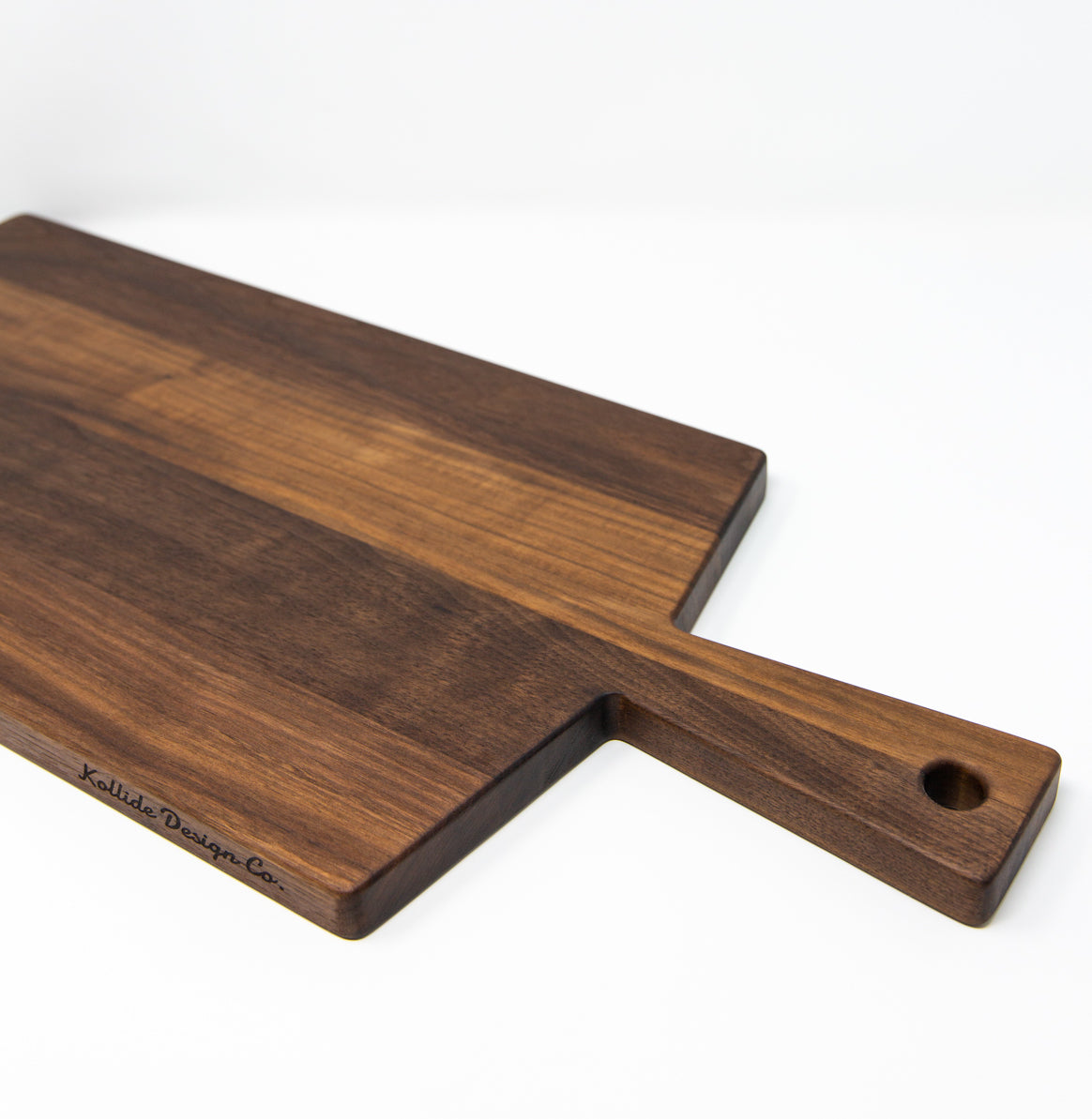 Large size wood charcuterie board, made of dark Walnut, with a slightly tapered handle and a long rectangular body.