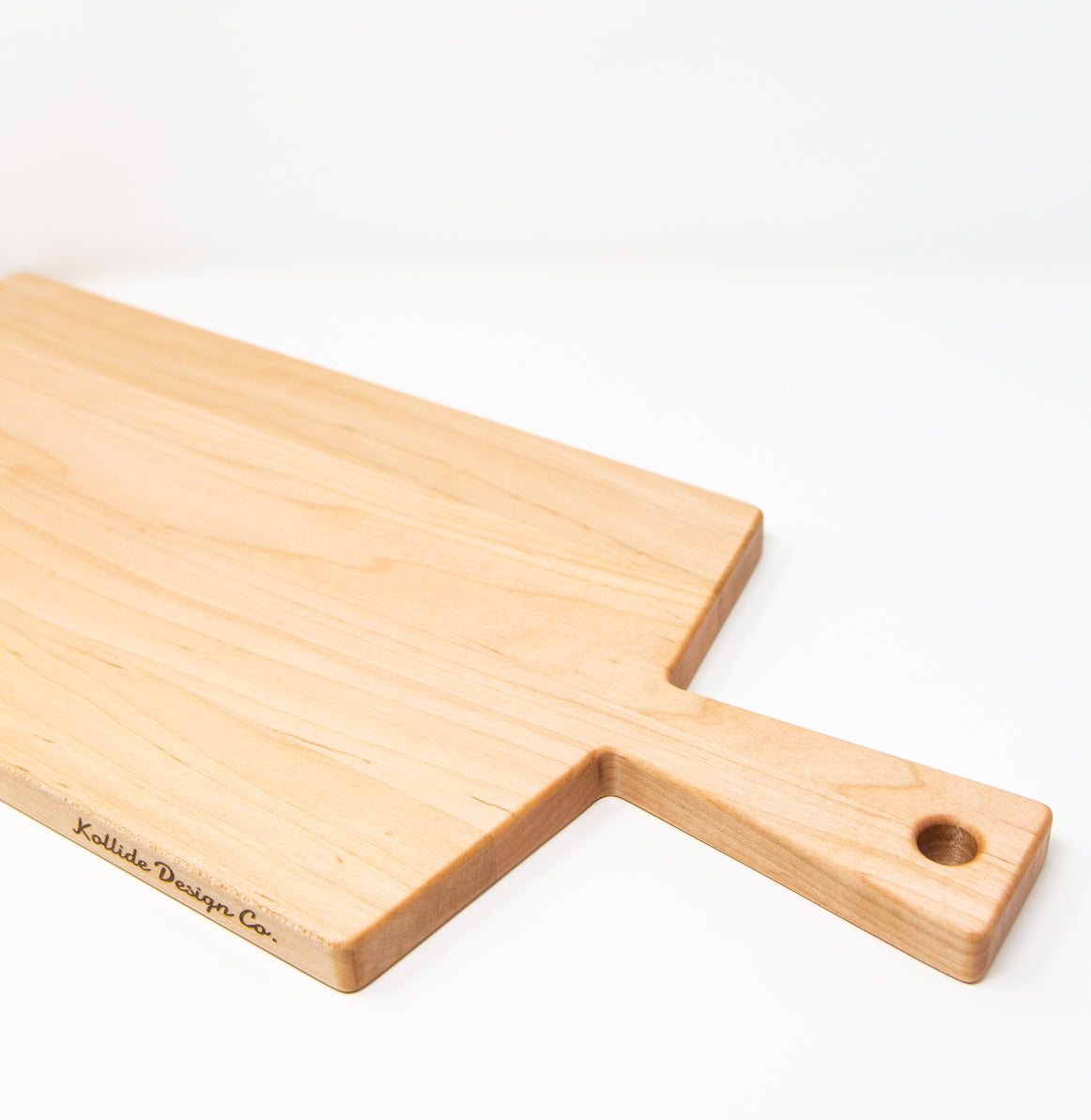 Large size wood charcuterie board, made of light blonde Maple, with a slightly tapered handle and a long rectangular body.