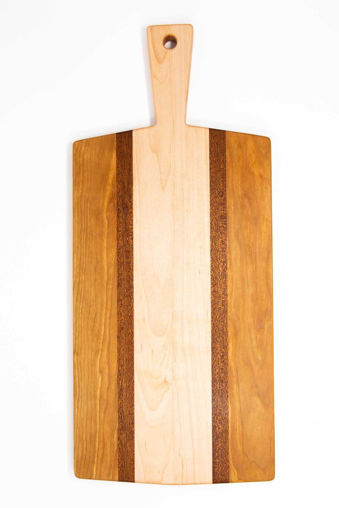 Large size wood charcuterie board, made of golden-brown Cherry, reddish brown Sapele and a center piece of light blonde Maple with a slightly tapered handle and a long rectangular body.