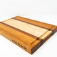 Large size wood cutting board, made of golden-brown Cherry, dark reddish-brown Sapele and light blonde Maple, with a juice groove and side handles.