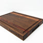 Extra large wood cutting board, made of dark walnut and two strips of dark reddish brown Bubinga, with a juice groove and side handles.