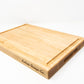 Medium size wood cutting board, made of light blonde Maple, with a juice groove and side handles.