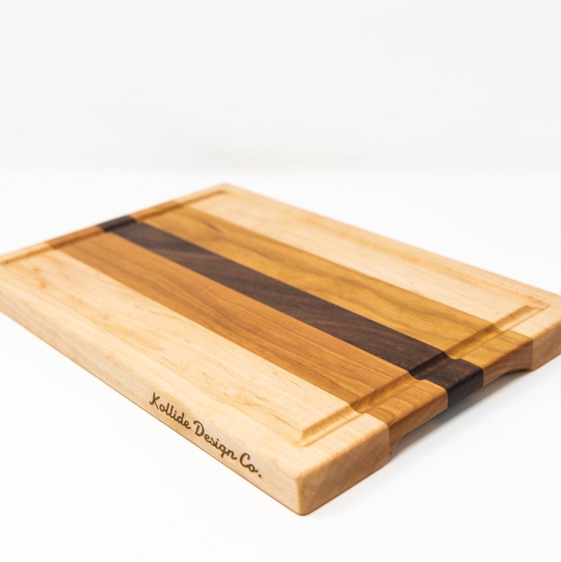 Small wood cutting board, made of light blonde Maple, golden-brown Cherry and a center strip of dark Walnut, with a juice groove and side handles.