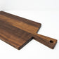 Large size wood charcuterie board, made of dark Walnut, with a slightly tapered handle and a long rectangular body.
