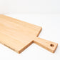 Large size wood charcuterie board, made of light blonde Maple, with a slightly tapered handle and a long rectangular body.