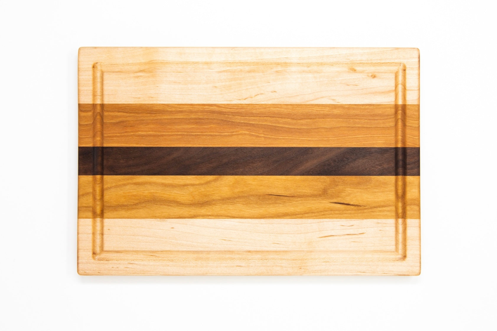 Small wood cutting board, made of light blonde Maple, golden-brown Cherry and a center strip of dark Walnut, with a juice groove and side handles.