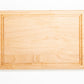 Small wood cutting board, made of light blonde Maple, with a juice groove and side handles.